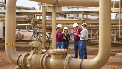 Collier central gathering facility, near Pecos, Texas. View of workers talking in the facility, framed by pipes.