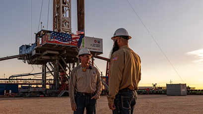 Two men talking to each other in front of an electric drilling rig at sunrise, in Carlsbad, New Mexico.